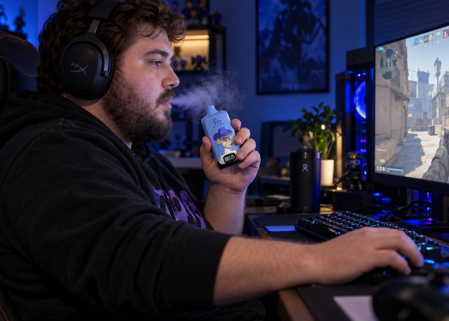Mann mit Kopfhörern sitzt am Gaming-PC und hält eine Fumot Digital Box 12000 in Blueberry On Ice